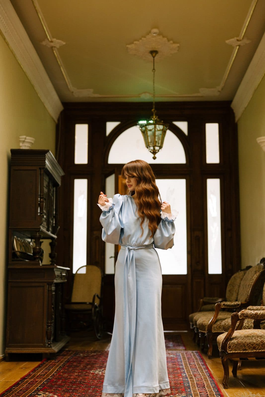Rochie lungă din satin bleu, într-un hol cu covor oriental