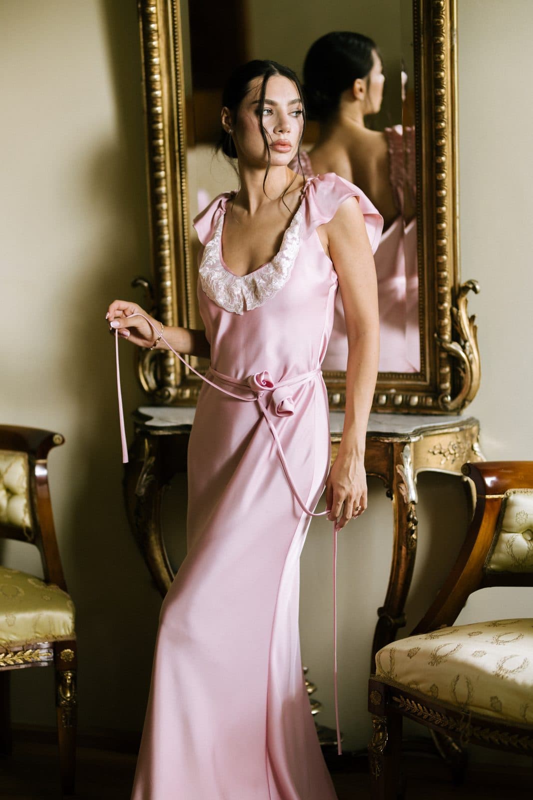 Rochie lungă din satin roz, purtată într-un interior cu oglindă și mobilier de epocă